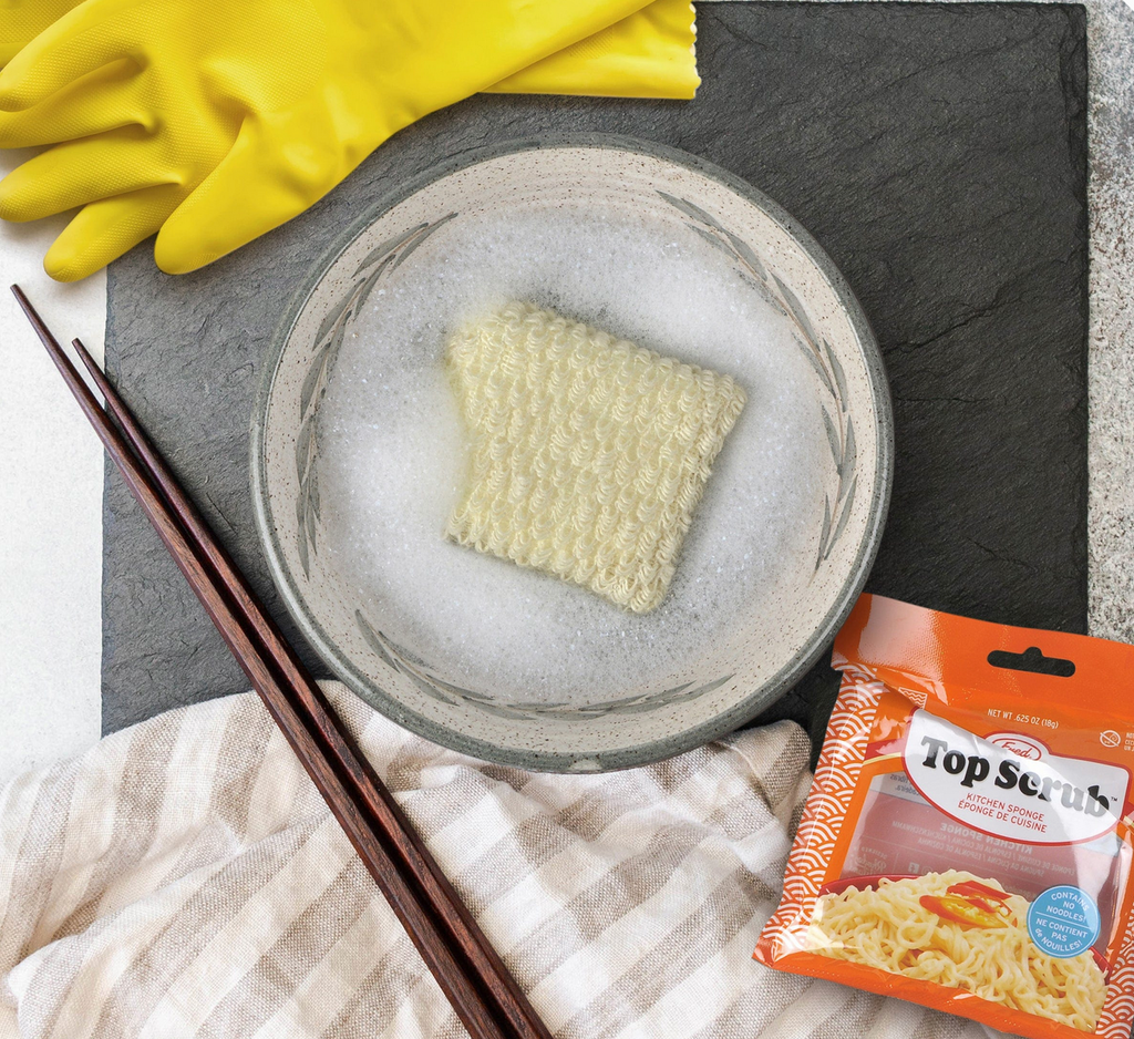 Top Scrub kitchen sponge in a bowl of water next to cleaning gloves, chopsticks, and package.