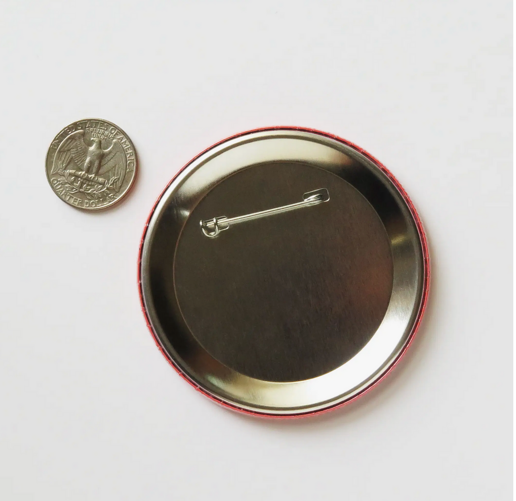The back side of the the round pinback button. The size is also compared to a quarter coin.  