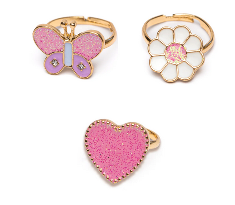 A close up of the three adjustable rings in the Wonderland Set. There is a pink glitter heart shaped ring, a flower with white petals and glittery pink center, and a butterfly with glittery pink and purple wings.